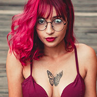 A woman with red hair and glasses wearing a bra.